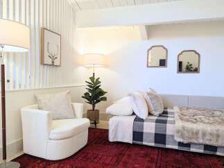 This cozy living space features a comfortable white armchair and a stylish daybed adorned with a buffalo check blanket and a plush faux fur throw.
