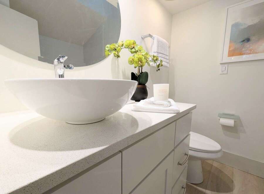 This modern bathroom features a sleek vanity with a white vessel sink and a chrome faucet, complemented by a large round mirror.