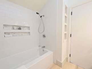 This modern bathroom features a sleek white subway tile shower and tub surround, complemented by built-in niches for convenient storage.