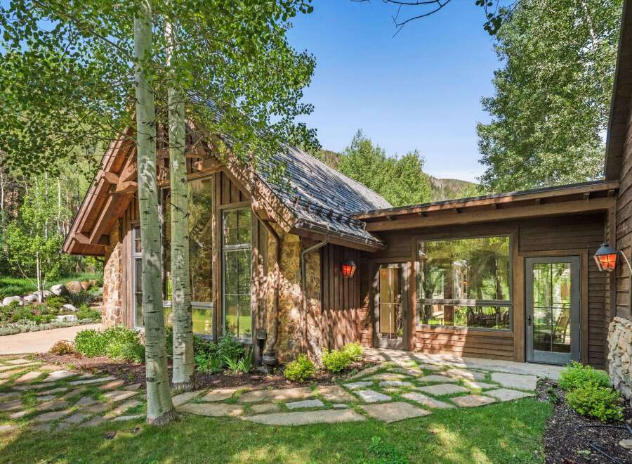 Experience rustic charm and modern luxury in this stunning mountain home, featuring a striking stone and wood exterior nestled amongst aspen trees.