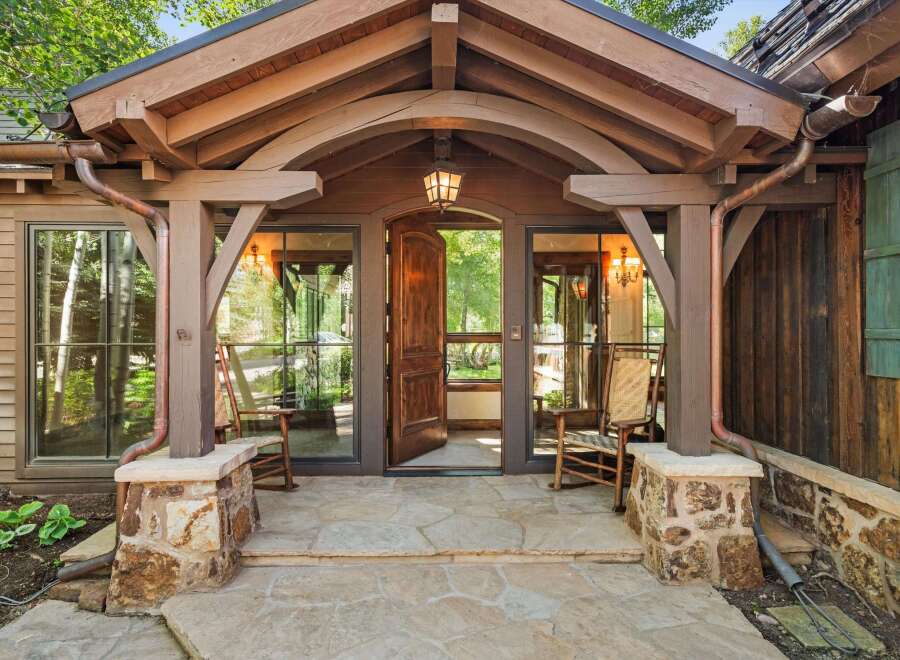 Step into this charming mountain retreat through a grand wooden door, flanked by inviting rocking chairs on a flagstone porch.