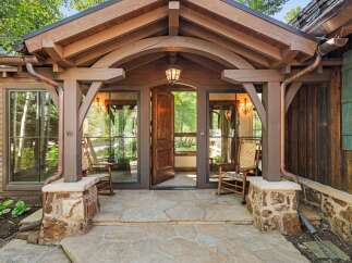 Step into this charming mountain retreat through a grand wooden door, flanked by inviting rocking chairs on a flagstone porch.