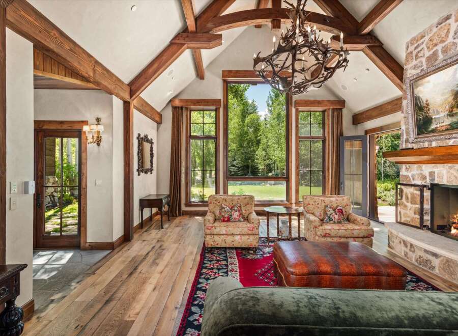 Experience rustic luxury in this stunning living room, featuring soaring vaulted ceilings with exposed wooden beams and a grand stone fireplace.