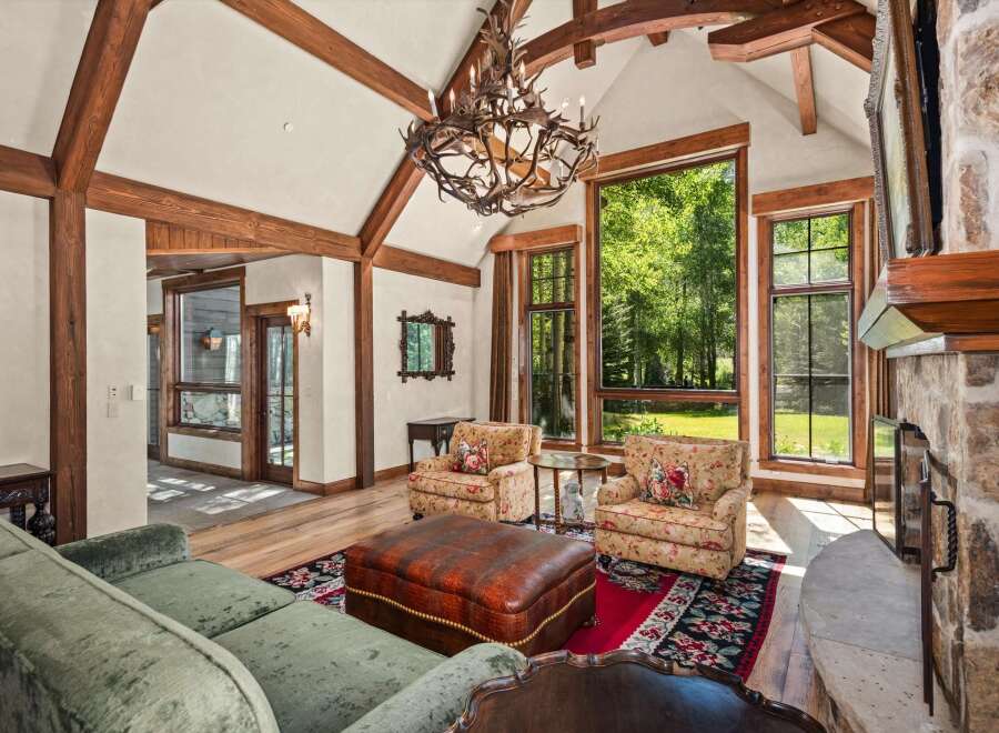 Experience rustic elegance in this stunning living room, featuring soaring vaulted ceilings with exposed wooden beams and a grand antler chandelier.