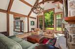 Experience rustic elegance in this stunning living room, featuring soaring vaulted ceilings with exposed wooden beams and a grand antler chandelier.