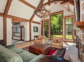 Experience rustic elegance in this stunning living room, featuring soaring vaulted ceilings with exposed wooden beams and a grand antler chandelier.