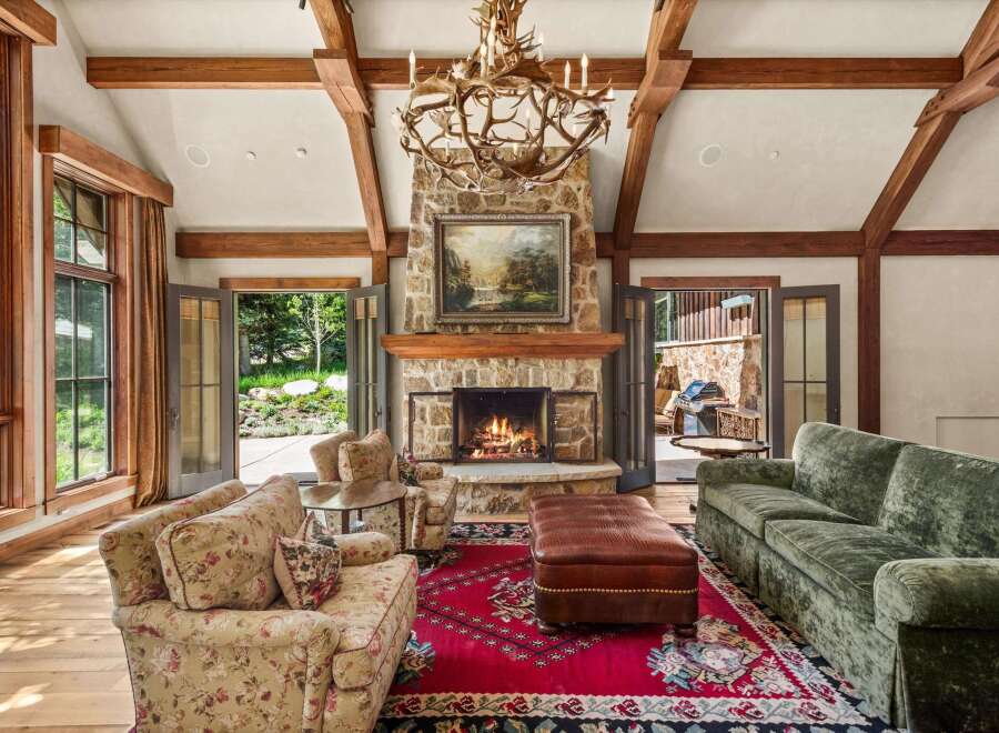 Experience rustic elegance in this stunning living room, featuring a grand stone fireplace and a unique antler chandelier.