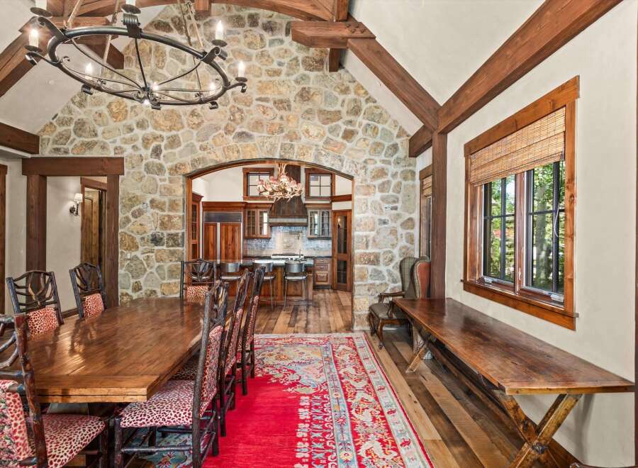 Experience rustic elegance in this stunning dining room, featuring a grand stone accent wall and exposed wooden beams that create a warm, inviting atmosphere.