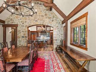 Experience rustic elegance in this stunning dining room, featuring a grand stone accent wall and exposed wooden beams that create a warm, inviting atmosphere.