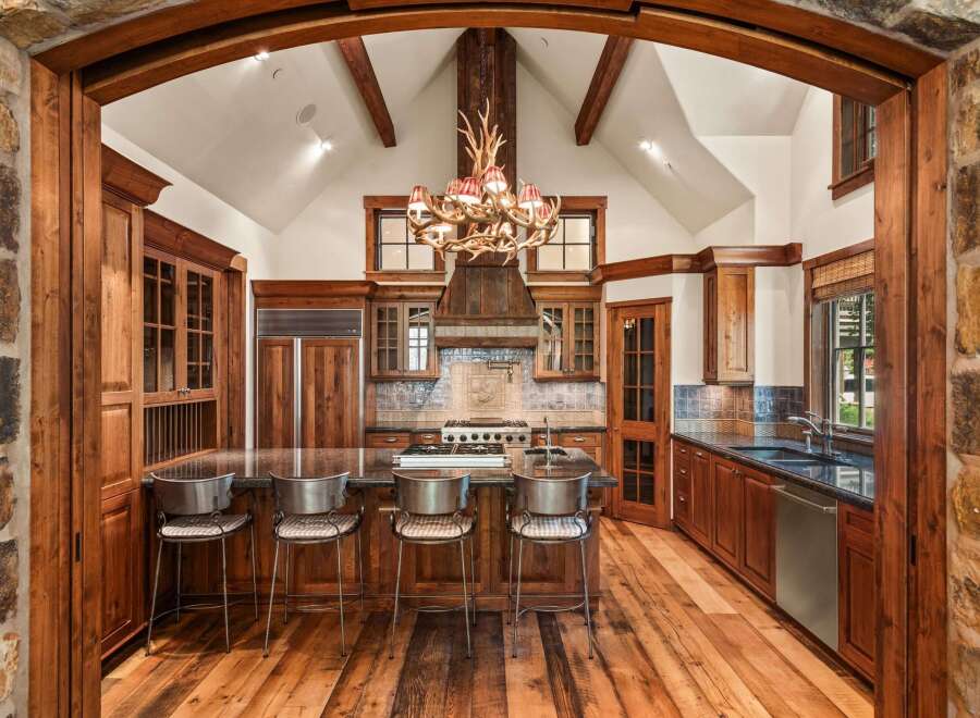 Experience rustic luxury in this stunning mountain kitchen, featuring a grand antler chandelier and a vaulted ceiling with exposed wooden beams.