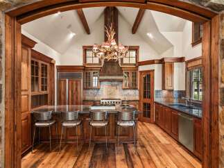 Experience rustic luxury in this stunning mountain kitchen, featuring a grand antler chandelier and a vaulted ceiling with exposed wooden beams.