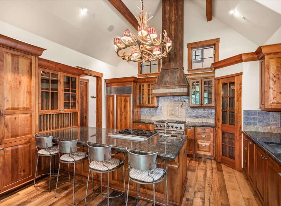 Experience rustic luxury in this stunning mountain kitchen, featuring custom wood cabinetry, a grand antler chandelier, and a spacious granite island with bar seating.