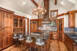 Experience rustic luxury in this stunning mountain kitchen, featuring custom wood cabinetry, a grand antler chandelier, and a spacious granite island with bar seating.