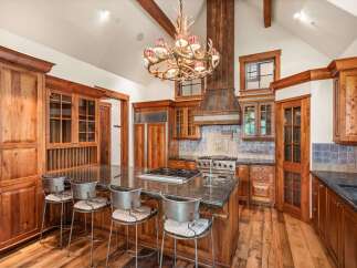 Experience rustic luxury in this stunning mountain kitchen, featuring custom wood cabinetry, a grand antler chandelier, and a spacious granite island with bar seating.