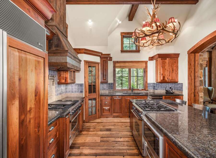 Experience rustic luxury in this stunning mountain kitchen, featuring custom wood cabinetry and a grand antler chandelier.