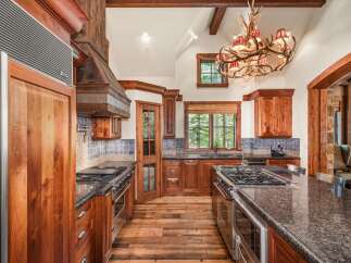 Experience rustic luxury in this stunning mountain kitchen, featuring custom wood cabinetry and a grand antler chandelier.