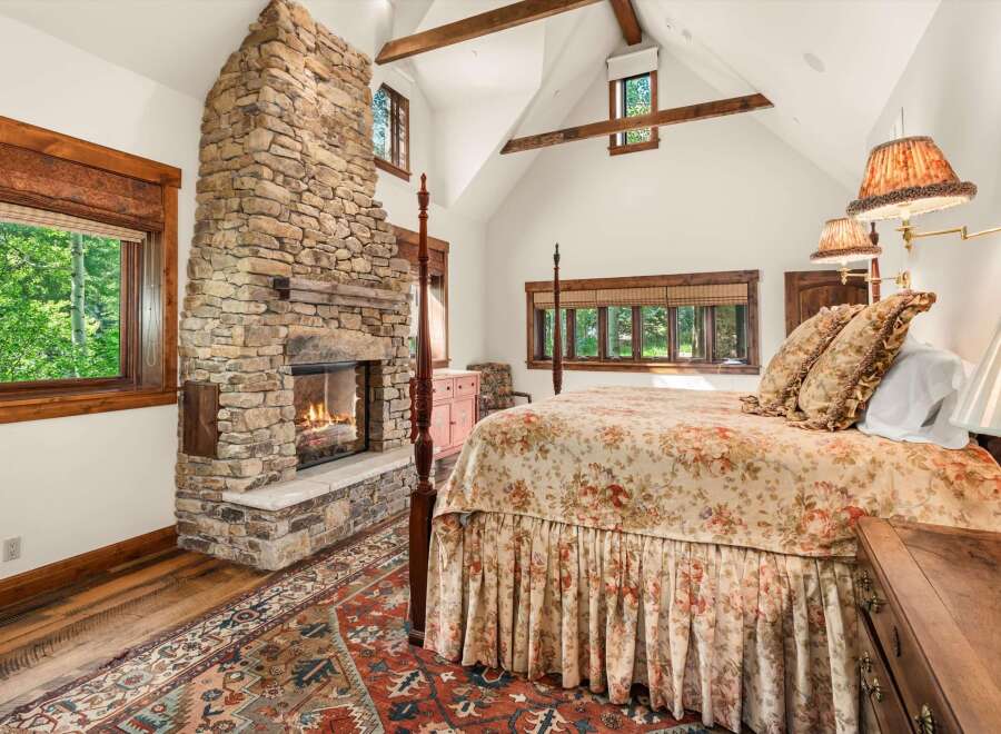 Experience rustic luxury in this charming bedroom featuring a grand stone fireplace and a cozy four-poster bed adorned with floral linens.