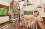 Experience rustic luxury in this charming bedroom featuring a grand stone fireplace and a cozy four-poster bed adorned with floral linens.
