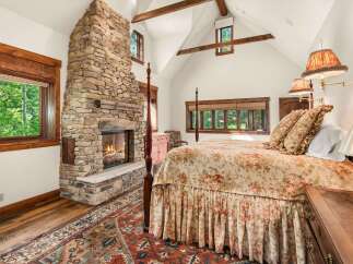 Experience rustic luxury in this charming bedroom featuring a grand stone fireplace and a cozy four-poster bed adorned with floral linens.