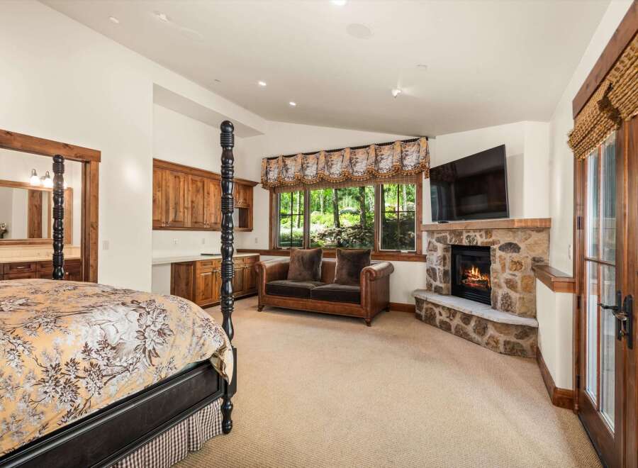 Experience rustic luxury in this spacious bedroom featuring a grand four-poster bed and a cozy stone fireplace.