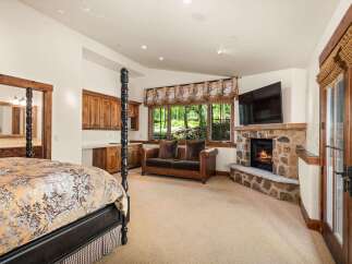 Experience rustic luxury in this spacious bedroom featuring a grand four-poster bed and a cozy stone fireplace.