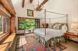 Experience rustic elegance in this charming bedroom, featuring a grand four-poster bed adorned with decorative pillows and a scenic bed skirt.