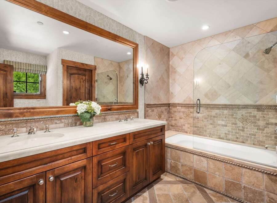 This luxurious bathroom features a spacious double vanity with a wooden cabinet and a stone countertop, complemented by elegant chrome fixtures.