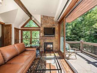 Experience luxurious living in this stunning mountain retreat, featuring a cozy stone fireplace and a spacious leather sofa perfect for relaxing.