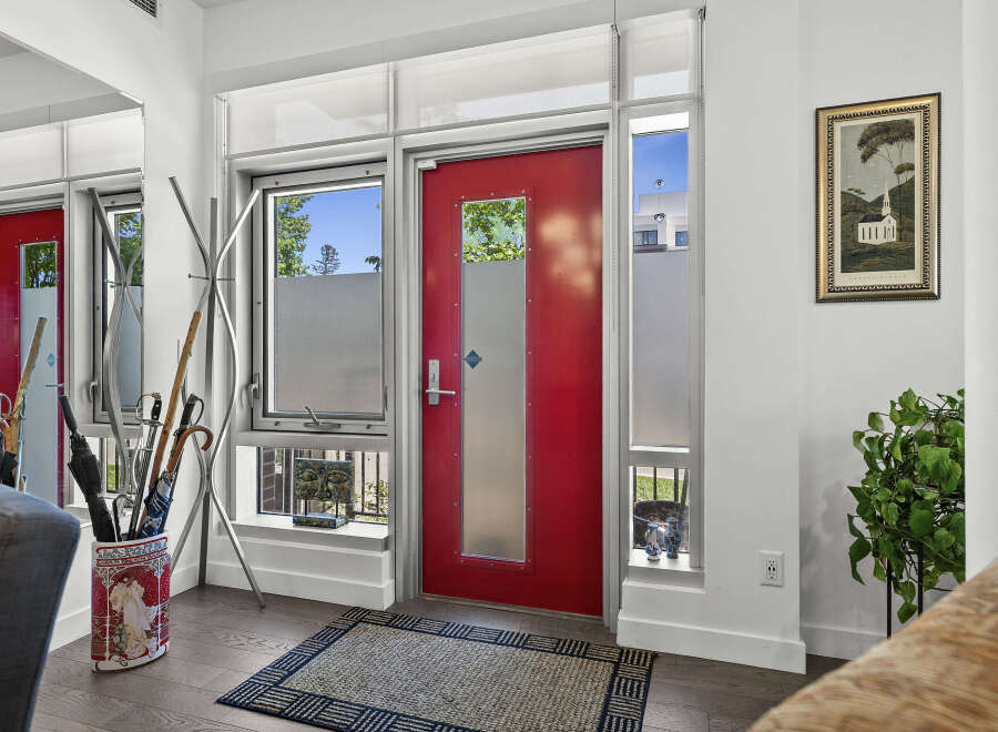 Welcome guests into this stylish entryway featuring a vibrant red door and ample natural light from the surrounding windows.