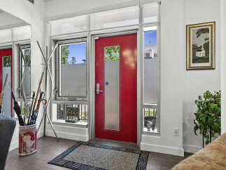 Welcome guests into this stylish entryway featuring a vibrant red door and ample natural light from the surrounding windows.