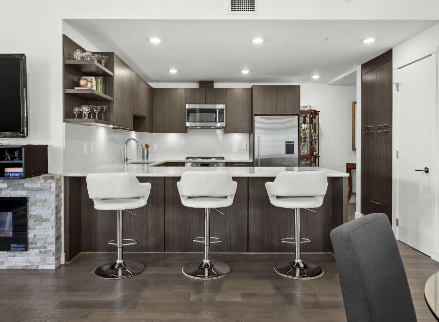 Experience modern living in this stunning kitchen featuring sleek dark wood cabinetry and a spacious quartz countertop island.