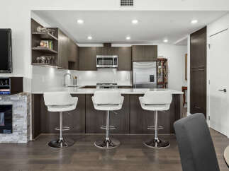 Experience modern living in this stunning kitchen featuring sleek dark wood cabinetry and a spacious quartz countertop island.