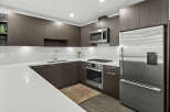 Experience modern living in this sleek kitchen, featuring dark wood cabinetry and pristine white quartz countertops.