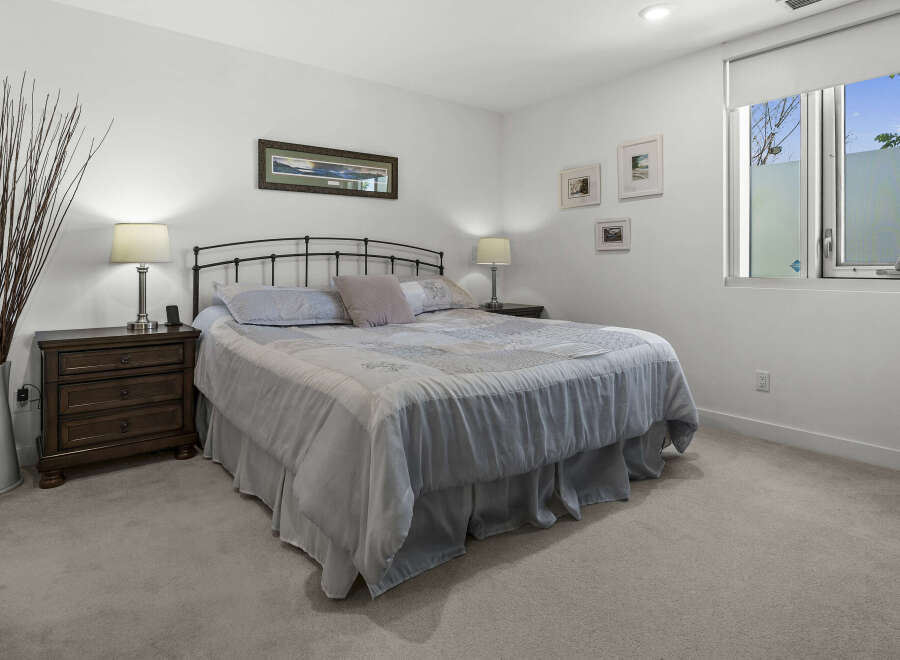 This serene bedroom features a comfortable queen-size bed with a light blue comforter and decorative pillows, complemented by a dark wood nightstand with a classic lamp.