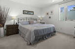 This serene bedroom features a comfortable queen-size bed with a light blue comforter and decorative pillows, complemented by a dark wood nightstand with a classic lamp.