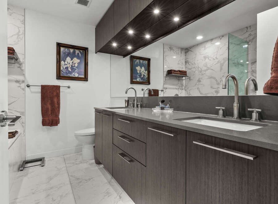 This luxurious bathroom features a sleek double vanity with modern cabinetry and a quartz countertop, complemented by elegant marble tilework.