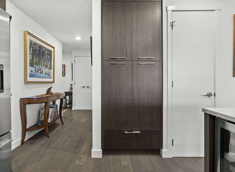 This modern hallway features a sleek, dark wood pantry with brushed nickel hardware, offering ample storage.