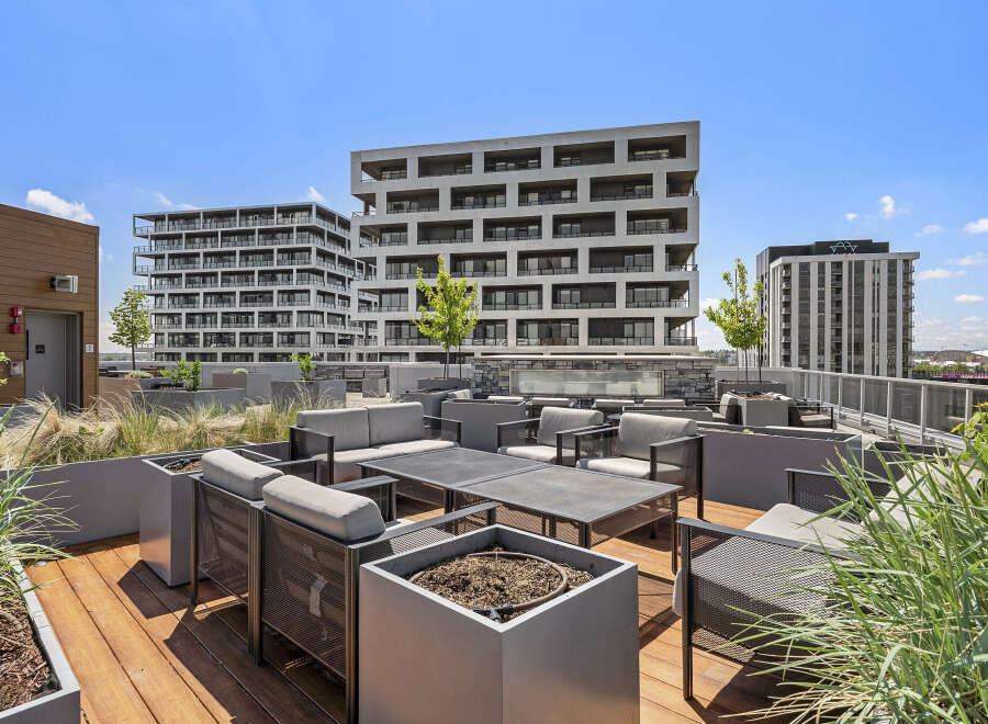 Experience modern urban living with this stunning rooftop patio, featuring comfortable seating and sleek planters.