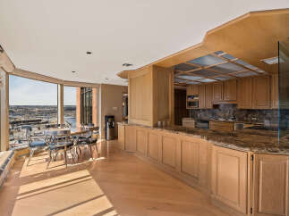 Experience breathtaking panoramic views from this stunning condo, featuring a spacious dining area with a table and chairs overlooking a cityscape and river.