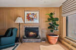 Cozy living room featuring a marble fireplace with a roaring fire, complemented by warm wood paneling and a vibrant abstract artwork.