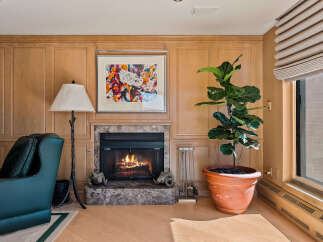 Cozy living room featuring a marble fireplace with a roaring fire, complemented by warm wood paneling and a vibrant abstract artwork.