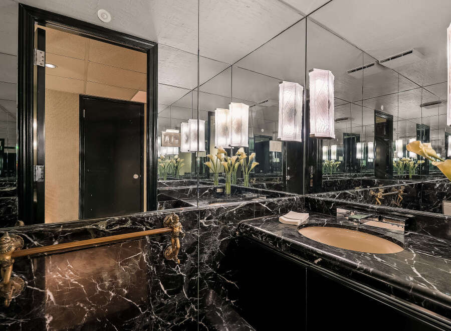 Experience opulent luxury in this stunning bathroom, featuring a sleek black marble vanity and a large mirrored wall that amplifies the space.