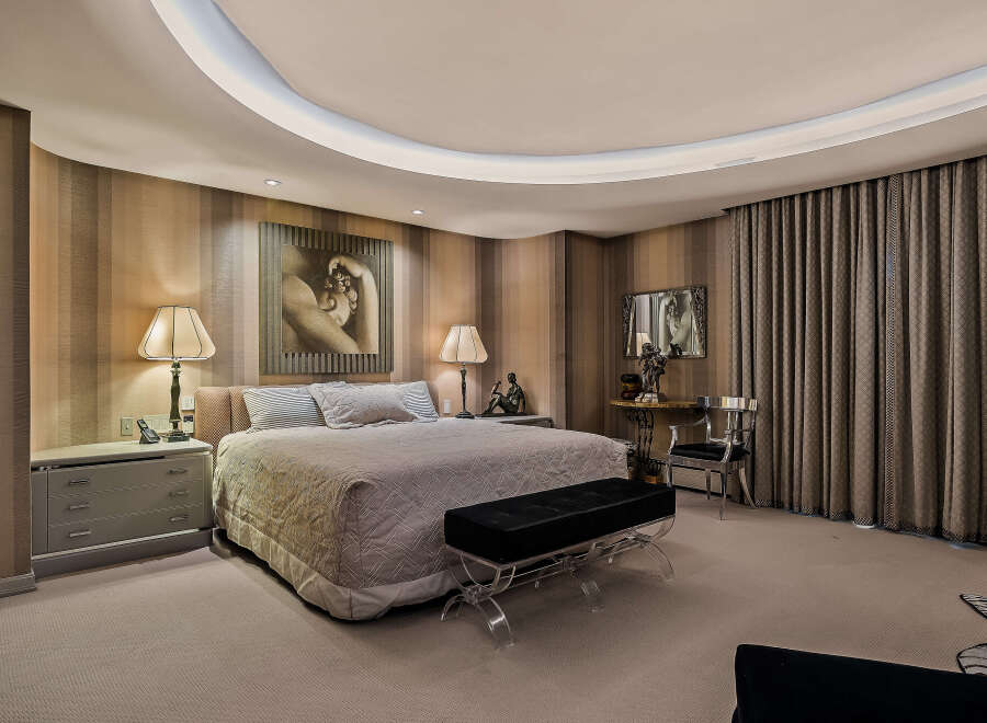 Experience luxury in this master suite featuring a king-sized bed with plush bedding and elegant striped wallpaper.
