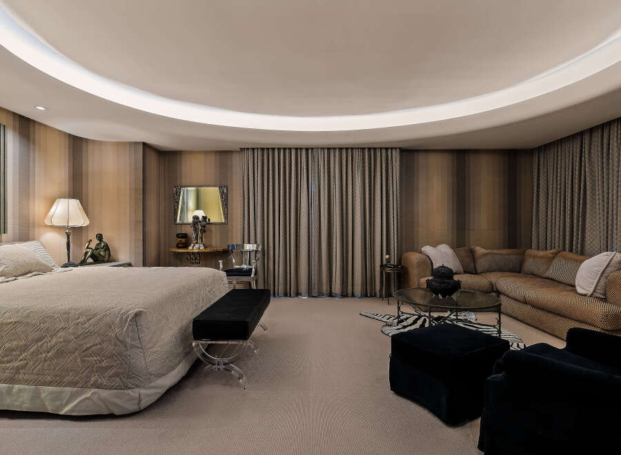 Experience luxurious living in this master suite, featuring a plush king-sized bed with a textured comforter and a chic black bench with acrylic legs.