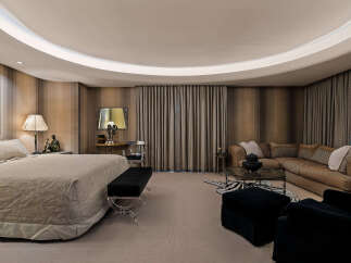 Experience luxurious living in this master suite, featuring a plush king-sized bed with a textured comforter and a chic black bench with acrylic legs.