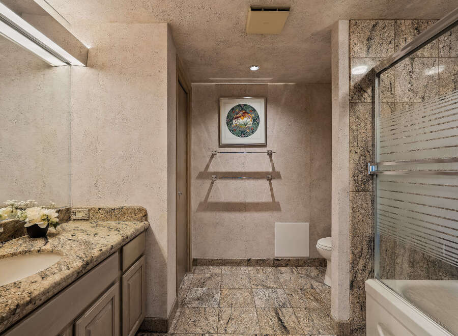 Experience luxury in this elegant bathroom featuring a granite-topped vanity with a vessel sink and a spacious shower-tub combination with frosted glass doors.