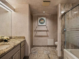 Experience luxury in this elegant bathroom featuring a granite-topped vanity with a vessel sink and a spacious shower-tub combination with frosted glass doors.