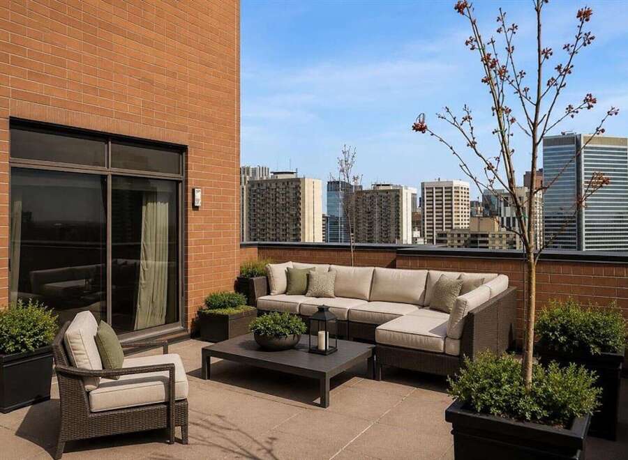 Experience luxurious urban living with this stunning rooftop patio, featuring a spacious sectional sofa and comfortable armchairs perfect for entertaining.