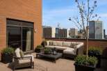 Experience luxurious urban living with this stunning rooftop patio, featuring a spacious sectional sofa and comfortable armchairs perfect for entertaining.