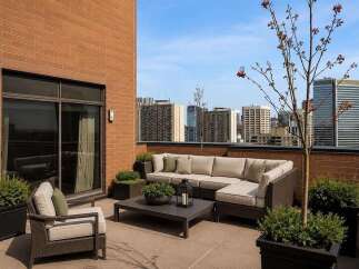 Experience luxurious urban living with this stunning rooftop patio, featuring a spacious sectional sofa and comfortable armchairs perfect for entertaining.